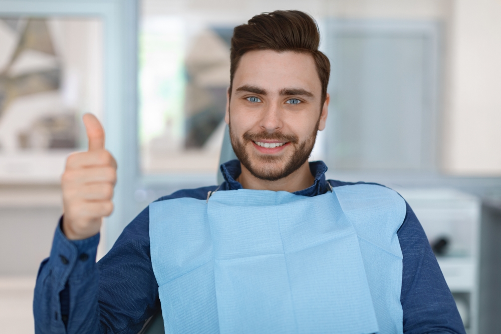 Smiling patient sitting in a dental chair giving a thumbs-up after successful treatment, symbolizing comfort and positive outcomes from oral surgery in Cupertino - Cupertino Oral Surgery