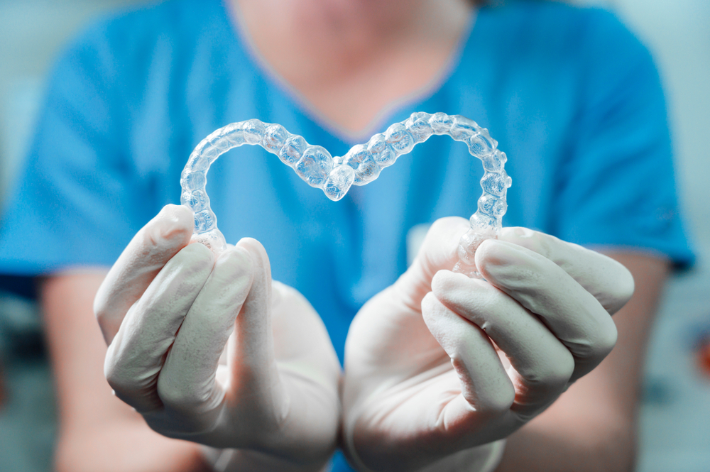 Dental professional holding clear aligners shaped like a heart, symbolizing patient care and advanced orthodontic treatment options with Invisalign in Cupertino - Invisalign Cupertino