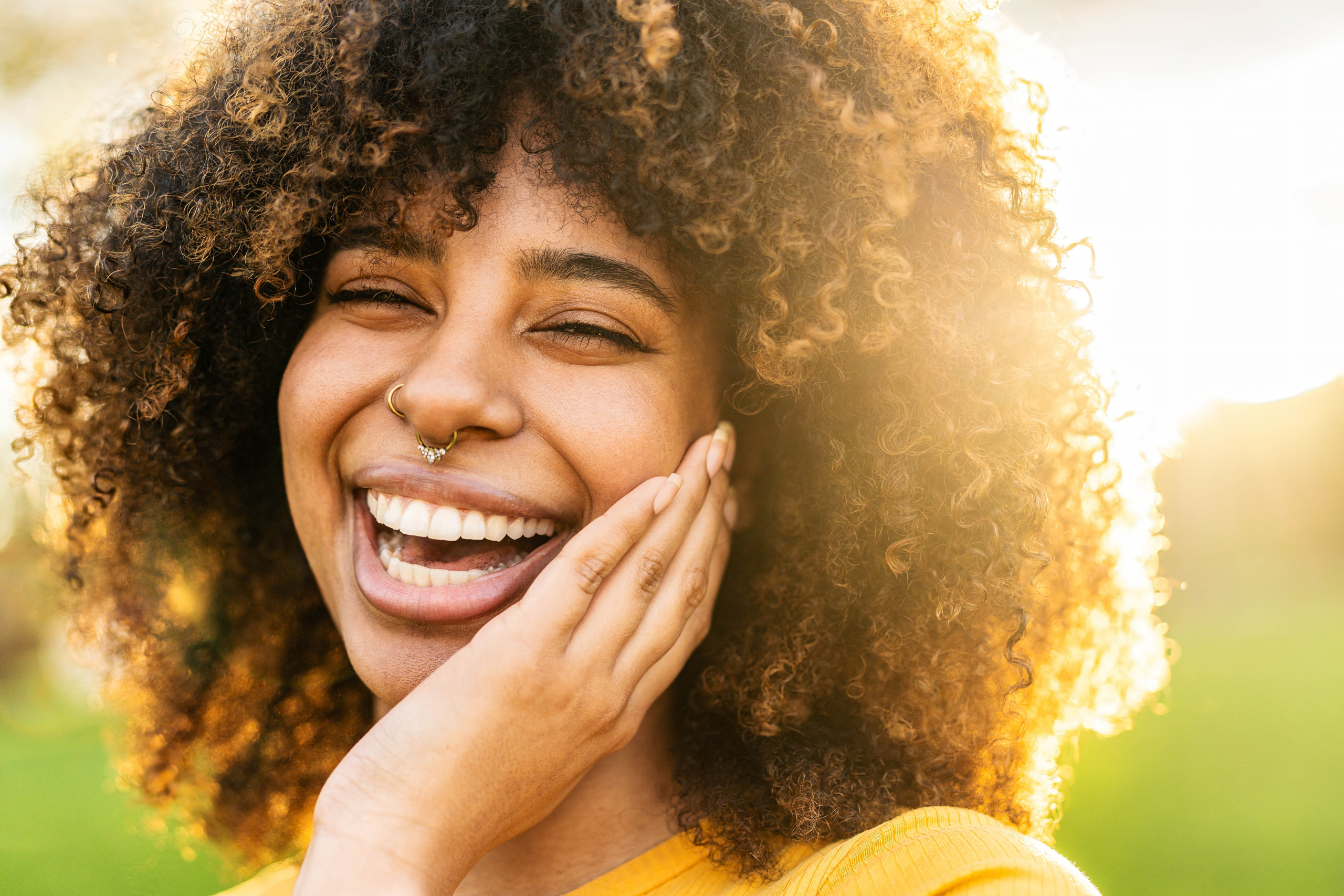 Portrait of a woman smiling brightly in natural sunlight, showcasing the aesthetic transformation and confidence possible with porcelain veneers in Cupertino - Porcelain Veneers in Cupertino