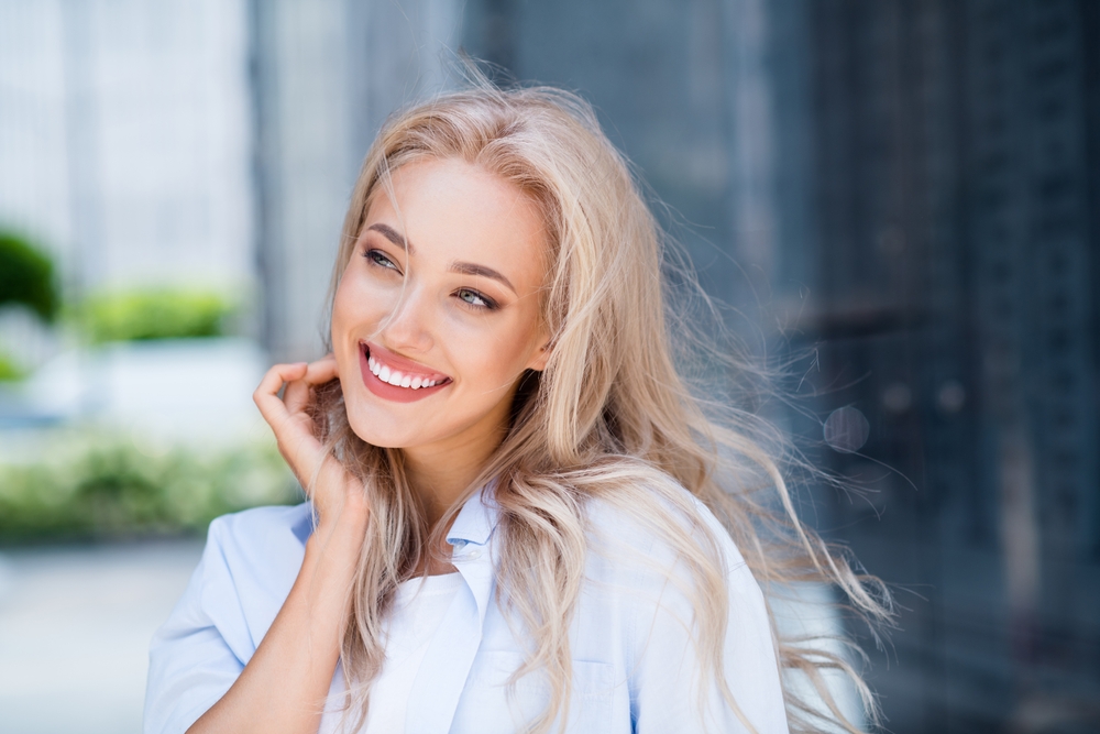 Smiling Woman Showing Beautiful Straight Teeth Outdoors - Cosmetic Dentist Cupertino Happy woman smiling with straight, radiant teeth in a bright outdoor setting, representing the confidence and aesthetic improvements offered by a cosmetic dentist in Cupertino - Cosmetic Dentist Cupertino