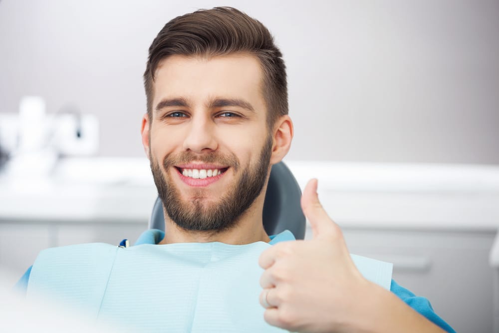 A smiling male patient in a dental chair wearing a bib, giving a thumbs-up gesture of approval - dentist Cupertino